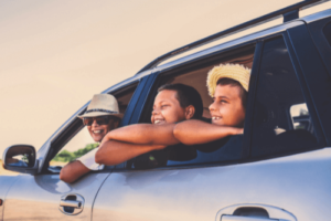 3 Pre Trip Maintenance Items You Don’t Want To Miss in Brooksville, FL with RDI Power. Image of smiling mother wearing sun hat and sunglasses leaning out of driver side window looking back at her tan sons that are also looking out of the window together smiling